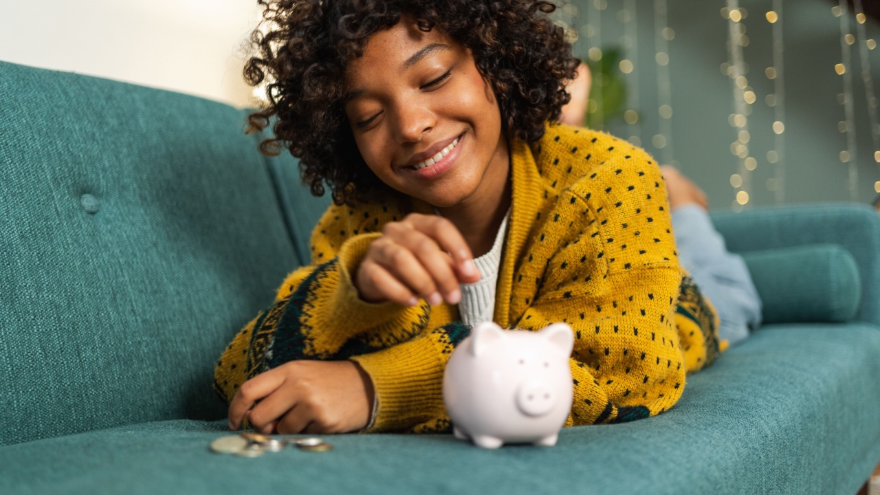 Saving money investment for future. African American girl putting money coin in pink piggy bank