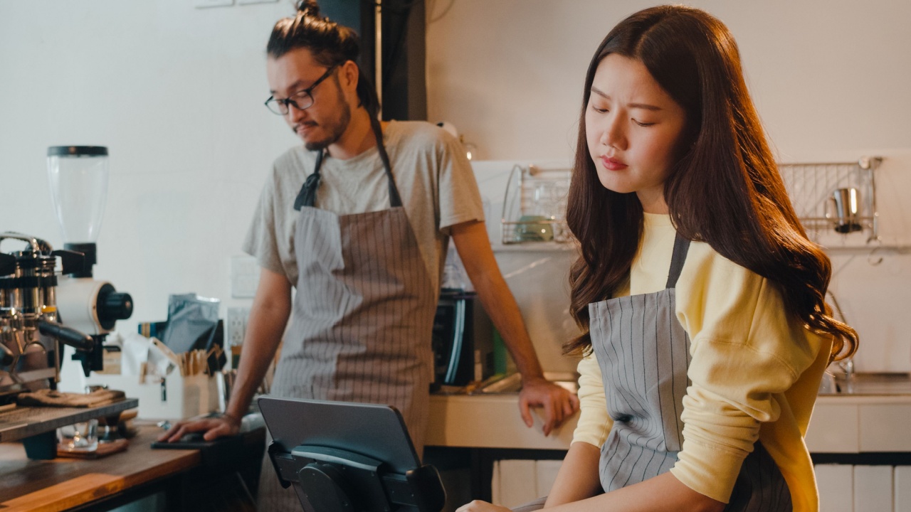 Young Asia female and male barista waiter overwhelmed by finance problems behind bar counter at cafe restaurant