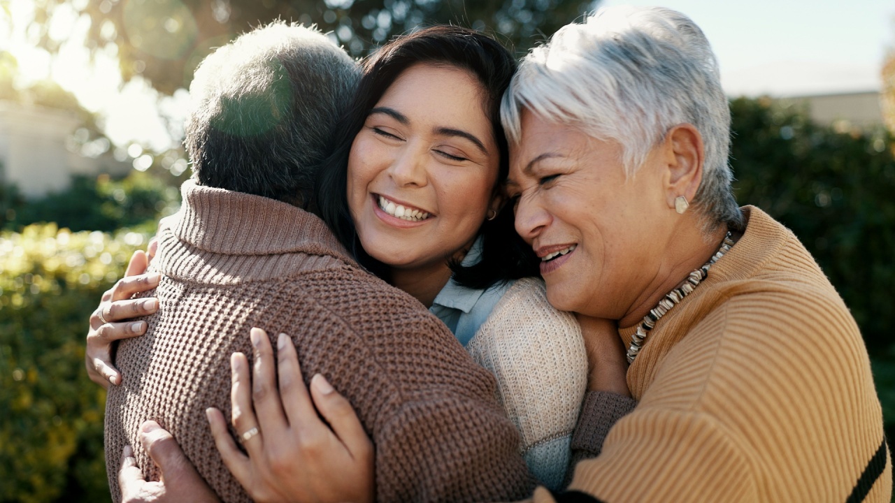 parents and adult daughter hugging and smiling outside