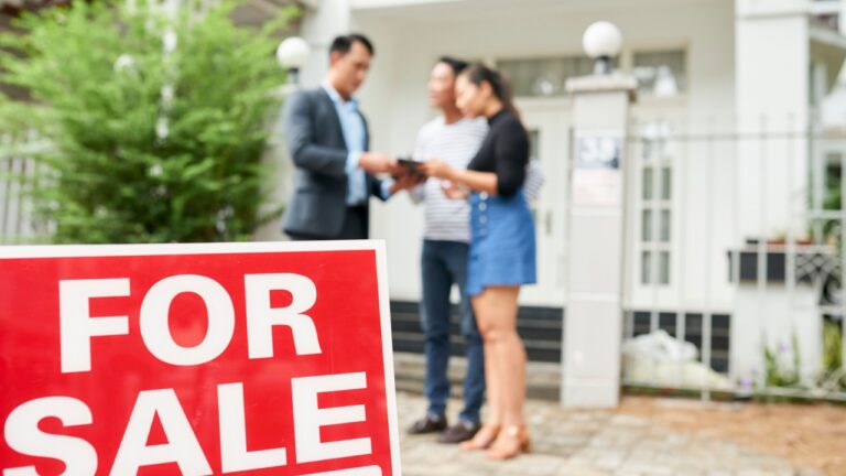 real estate agent and couple with For Sale sign