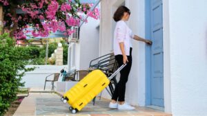 Outdoor, woman traveler with yellow suitcase opening closing door of the house